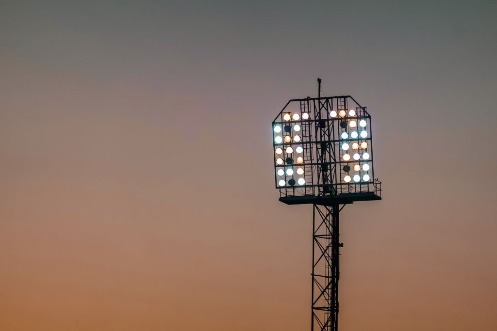 Flutlichtmast eines Sportplatzes vor orangefarbenem Abendhimmel
