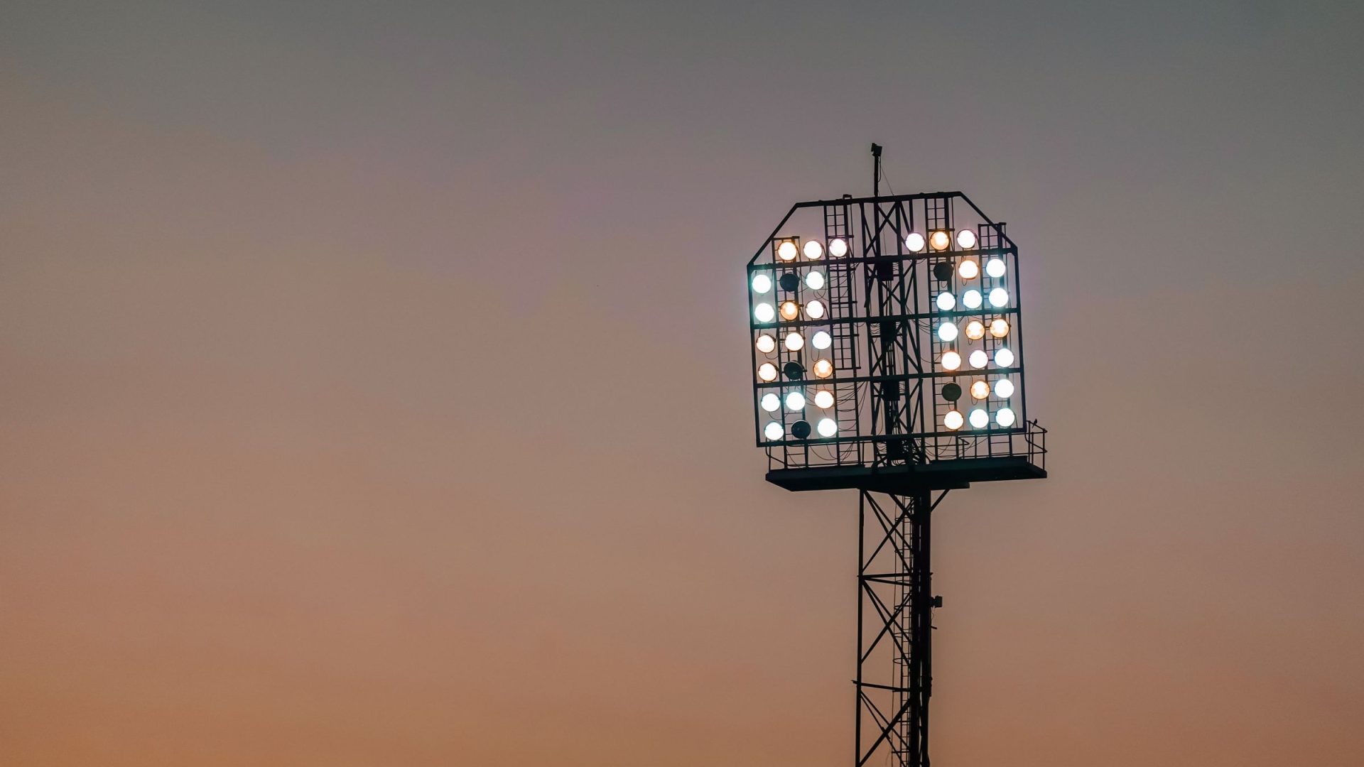 Flutlichtmast eines Sportplatzes vor orangefarbenem Abendhimmel